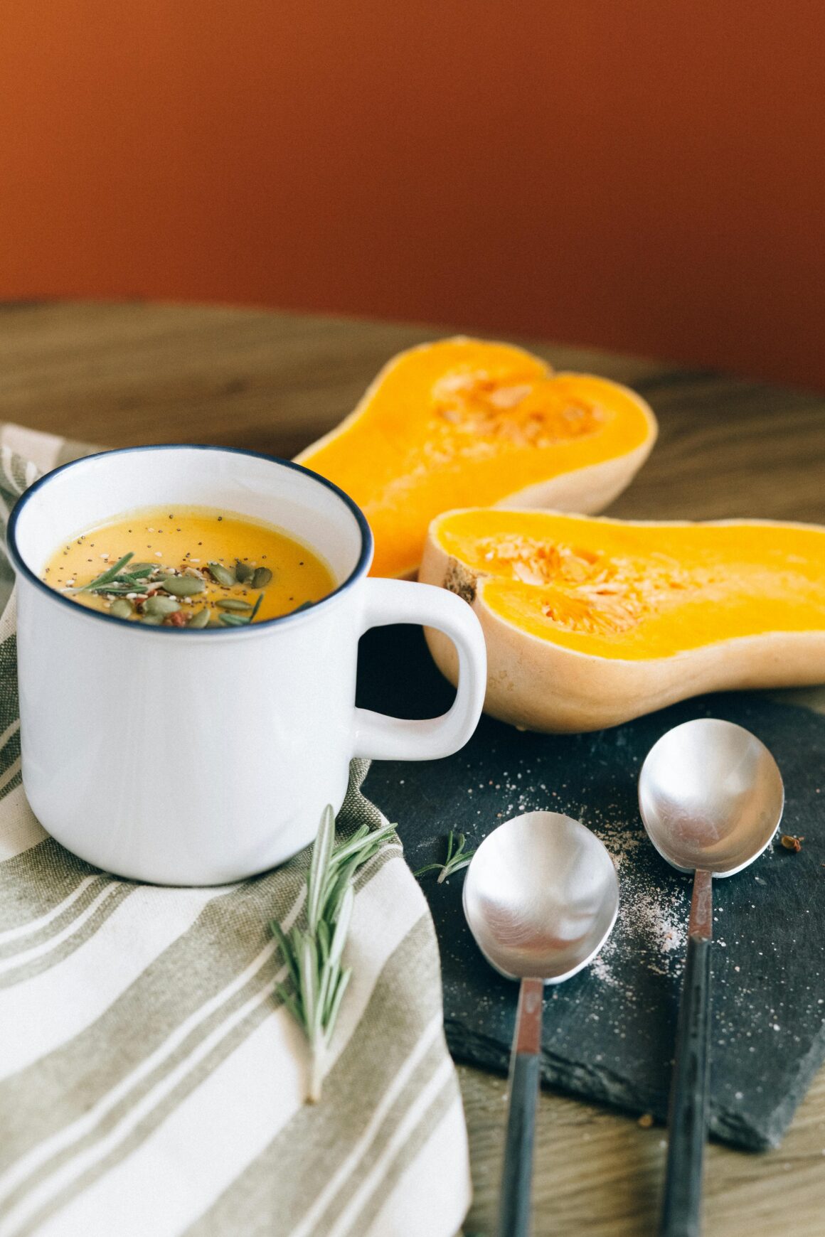 Warm butternut squash soup with rosemary garnish served in a cozy fall setting.